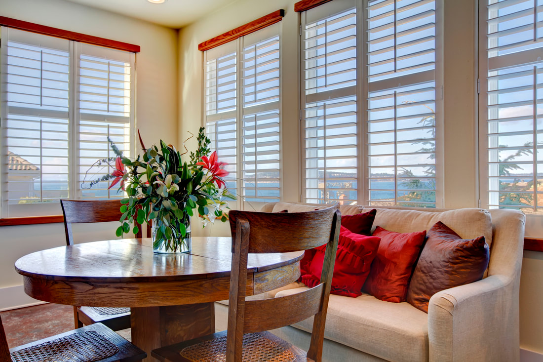 White plantation shutters surrounding a bright dining nook with a coastal view